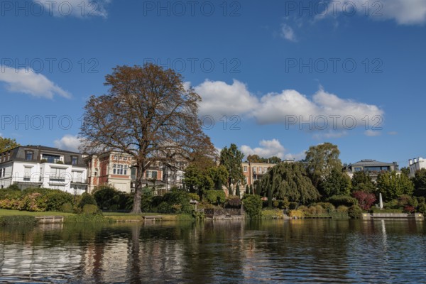Stylish townhouses reflected in the water, surrounded by lush autumn foliage, Alster, Hamburg, Germany