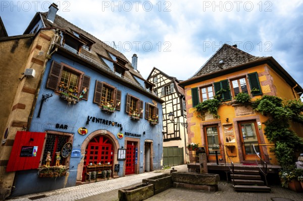 Colourful historic facades with cosy bars and restaurants under a cloudy sky. Alsace France