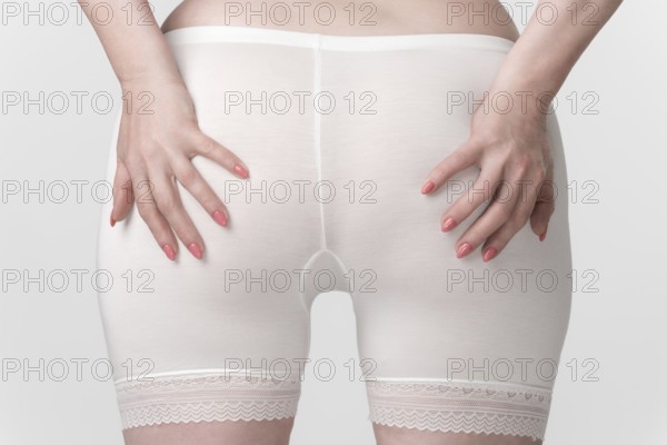 Woman's hips in pantaloons panties, back view of woman with her palms placed on her buttocks. Close-up of the midsection of an unrecognizable plus size female body. Women's health and wellness concept