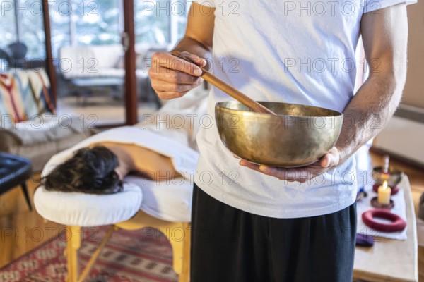 Man holding a bronze sound bowl with a stick, used for sound therapy and sound massages. A Professional massage therapist giving sound massage