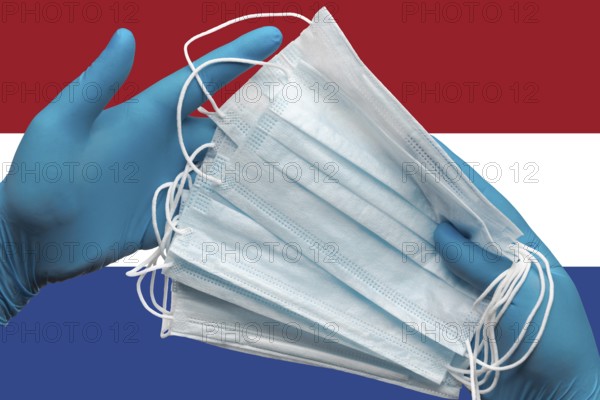 Doctor holds face masks in hands surgical blue gloves on background national flag of Netherlands. Concept pandemic outbreak, grippe, coronavirus quarantine, hygiene. Medical antibacterial face bandage
