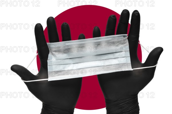 Doctor holds face mask in hands in black medical gloves on background colors flag of flag of Japan or Japanese flag. Pandemic insurance coronavirus, airborne diseases. Human respiratory medical mask