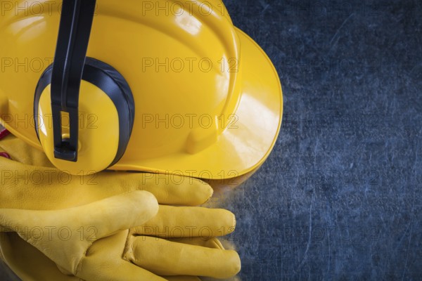 Hard hat ear muffs and leather protective gloves on metallic background close up view construction concept