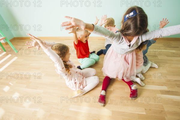 Kids with irresistable joy playing on a wooden floor at the preschool. Children full of fun and happiness holding their hands up