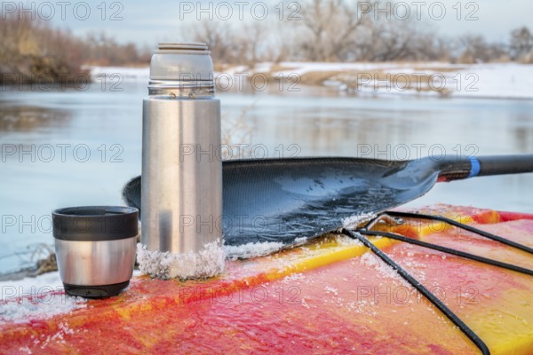 Winter kayaking in Colorado - thermos bottle with hot tea on the icy deck of a red whitewater kayak on shore of St Vrain Creek