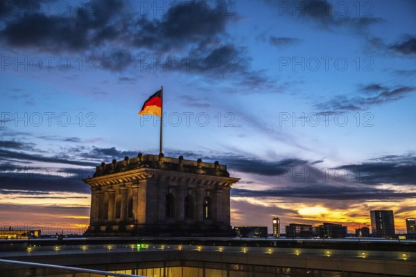 The Berlin Reichstag in the evening sky with the flag of Germany and clouds in the background. The Berlin Reichstag in the evening sky with the flag of Germany