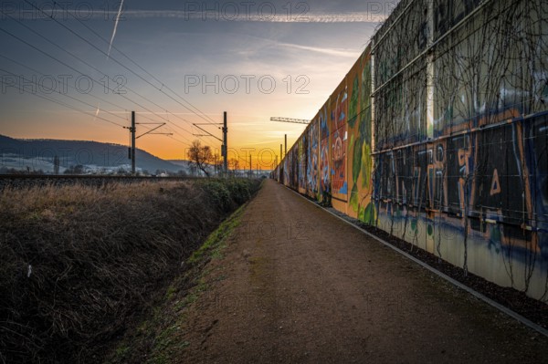 A path along a graffiti-covered wall at sunset, with rails and urban atmosphere, Jena, Thuringia, Germany