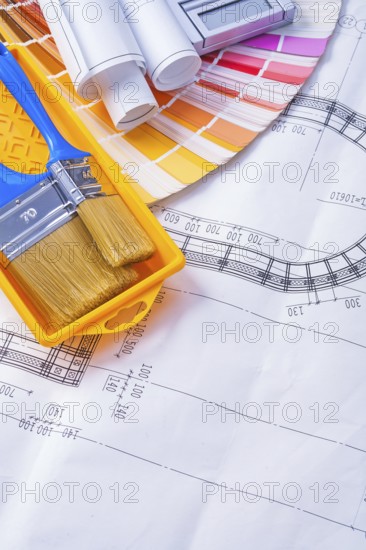 Paintbrushes in paint can and rolled blueprints on color pallete