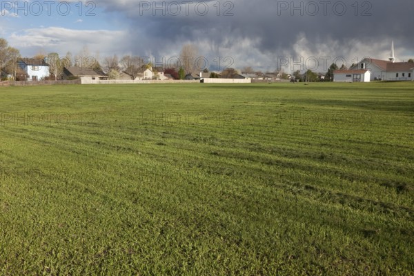Freshly mowed, large field of grass with residential homes, church and heavy storm clouds in background