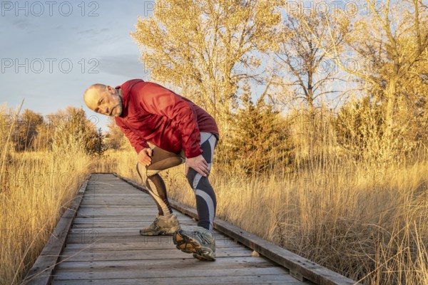 Senior male runner is stretching on a boardwalk trail, fall sunset at Riverbend Ponds, popular natural area in Fort Collins, Colorado for walking, jogging and running