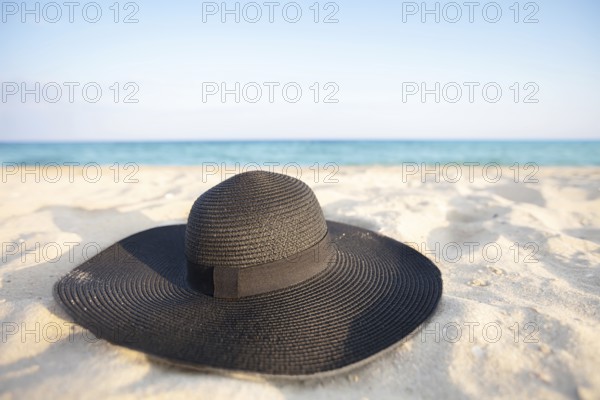 Black hat on a background of the sea. Beach accessory on white sand. Straw panama on the background of the ocean