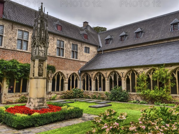 Small monastery courtyard with well-tended garden, Gothic arches and a central stone sculpture, Xanten, North Rhine-Westphalia, Germany