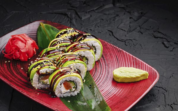Food, Delicious sushi rolls are beautifully arranged on a red plate. They feature fresh ingredients, topped with avocado and drizzled with sauce, accompanied by wasabi and pickled ginger