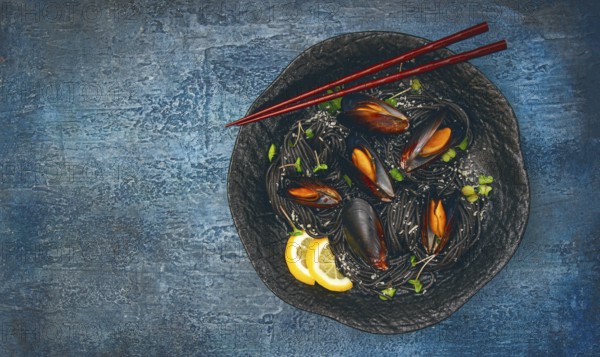 Spaghetti with black squid, black pasta, with boiled mussels, on a black plate, with parsley and parmesan cheese, close-up, selective focus, no people