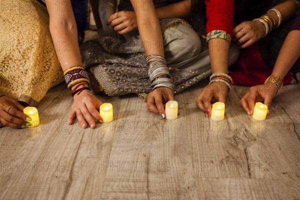 Women's hands holding lighted candles, sitting on floor. Indian holiday Diwali traditions. Closeup artificial candles on wooden floor. Nature saving concept