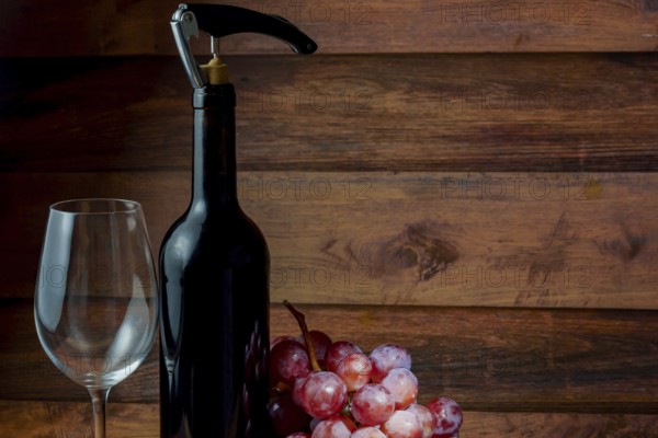 Wine bottle with corkscrew, empty wineglass and bunch of grapes on wooden background, ready for wine tasting