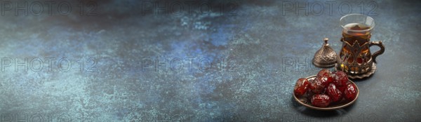Breaking fasting with dried dates during Ramadan Kareem, Iftar meal with dates and Arab tea in traditional glass, angle view on rustic blue background. Muslim feast, space for text, food photography, food photography