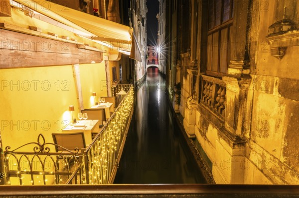Restaurant tables on a balcony above a canal, night shot, Venice, Italy