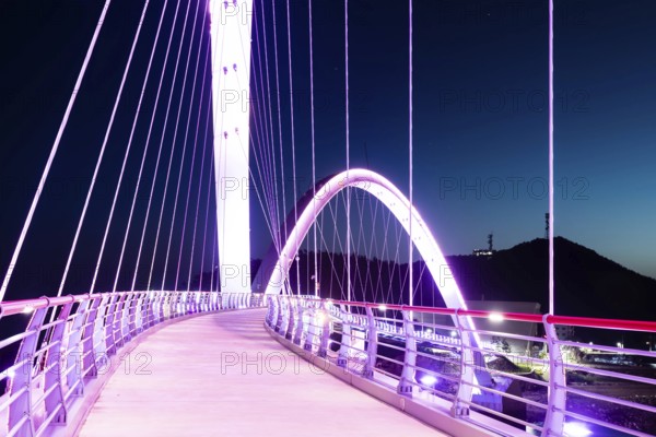 Pedestrian perspective on a suspension bridge illuminated with purple lights at night, in Sinjin-do, South Korea