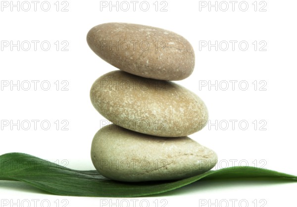 Stacked stones on base of green leafs. White isolated studio shot