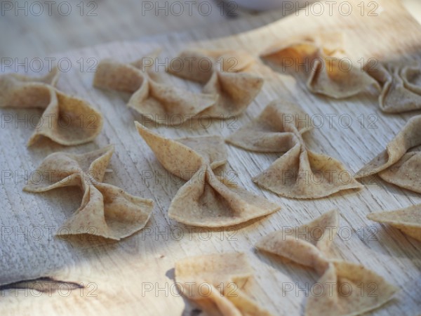 Fresh raw homemade whole-grain pasta in the shape of a bow, Farfalle, on a wooden board