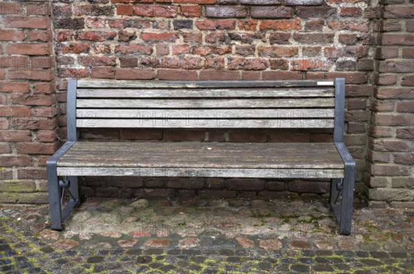 Empty wooden bench with metal frame sits against a weathered brick wall, inviting contemplation and rest