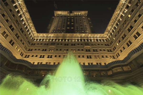 The jets of a fountain illuminated by green light before an enormous architectural complex in Hong Kong