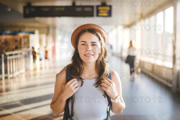 Theme tourism travel. Young beautiful Caucasian woman in dress and hat with backpack tourist mat in terminal station in a long walkway, the schedule board, the gate of the departure and the plane