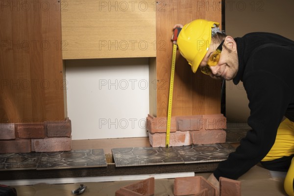 The construction worker looks at the camera and smiles while measuring. Wearing personal protective equipment