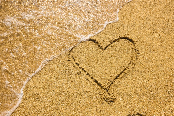 Heart symbol on the sand. Summer holiday concept. Romantic love background. Valentin Day theme. Top view. Heart drawn in sea beach sand, soft wave in a sunny day