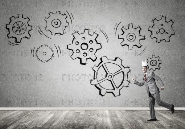 Young handsome businessman wearing white paper crown running and gear mechanism on wall