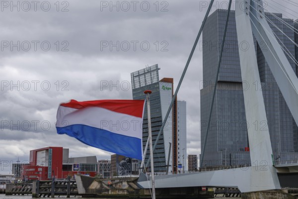 Dutch flag waving in front of a bridge and modern buildings under a cloudy sky, Rotterdam, Netherlands