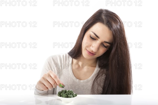 Beautiful happy healthy girl in her 20s with green dietary supplements chlorella, spirulina and wheatgrass pills isolated on white background. Detox, healthy living