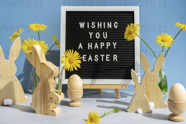 WISHING YOU A HAPPY EASTER text on letter board with bunny wooden figures and fresh flowers. Easter composition content still life. Christian symbols of spring holiday