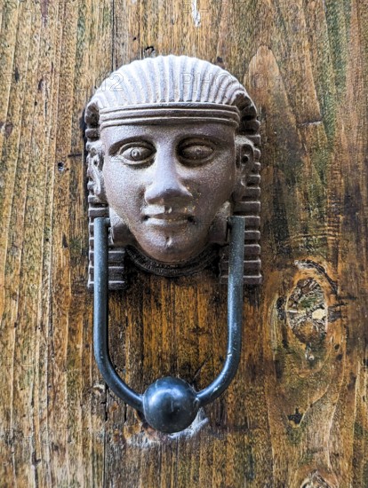 Vintage style doorknocker of an Egyptian head, a door in Italy