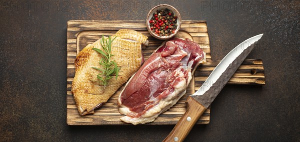 Two raw uncooked duck breast fillets with skin, seasoned with salt, pepper, rosemary top view on wooden cutting board with knife, dark brown concrete rustic background, food photography, food photography