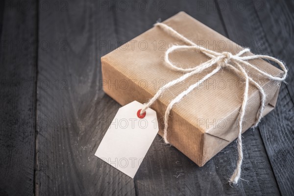 Gift box, wrapped in brown vintage paper and tied with white flax string, on an old black wooden table