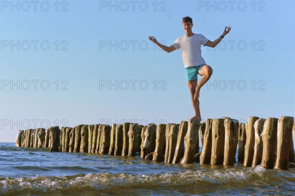 A young man stands on the breakwater, wooden breakwater, breakwater in the sea for protection from the storm