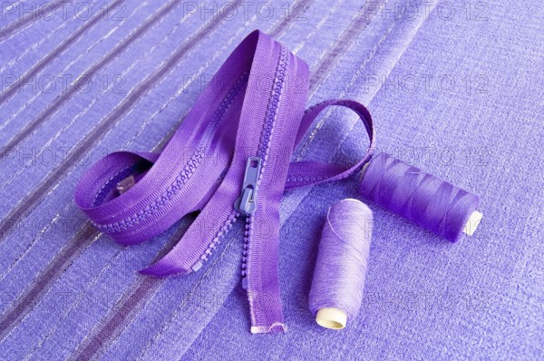 Locking zipper and two reels of thread on the purple plain and striped fabrics