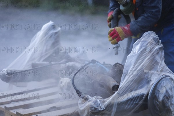 A worker in protective gloves sanding car parts covered in plastic, producing dust