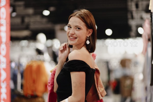 Woman smiling brightly, enjoying shopping among colorful clothes inside a store