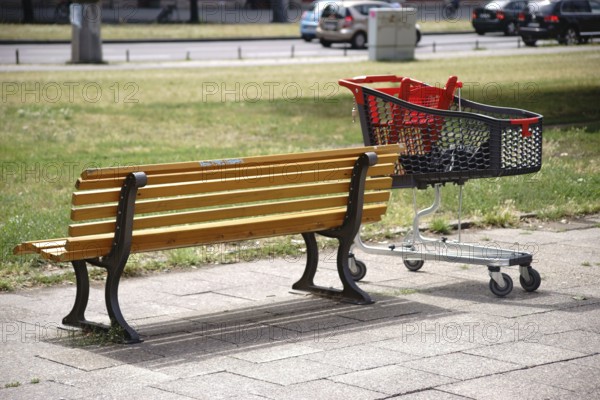 A modern plastic shopping trolley stands next to a park bench in the city