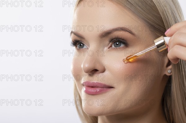 A woman gently applies a brightening serum to her face, promoting radiant and healthy skin with every touch