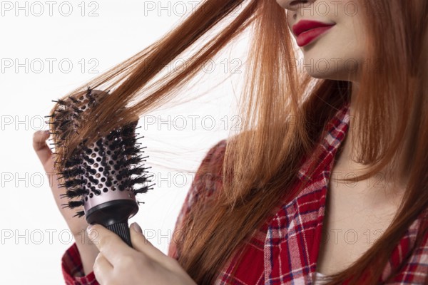 A woman is lovingly brushing her long, shiny hair with a round brush, showcasing her detailed haircare routine