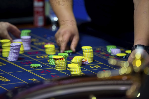 Roulette table with human hands putting down chips in casino. Roulette wheel in the foreground. Gamble game. Unrecognizable people