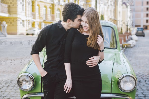 Young multiracial couple, male and female lovers heterosexual people students. Beautiful models posing standing near a retro car in the city. Dressed in black clothes