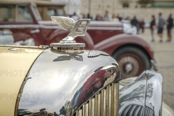 Lisbon, Portugal - Oct 15, 2023: Close-up and selective focus on the Bentley Wings Flying B mascot hood ornament or bonnet badge of 1930s against other car background