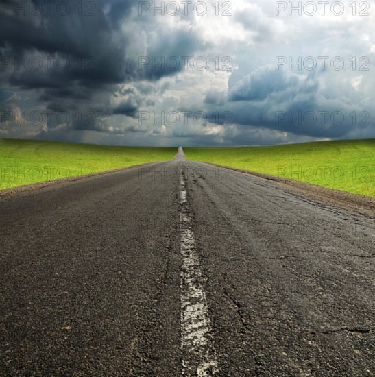 Old broken asphault road in green field over blue cloudy sky