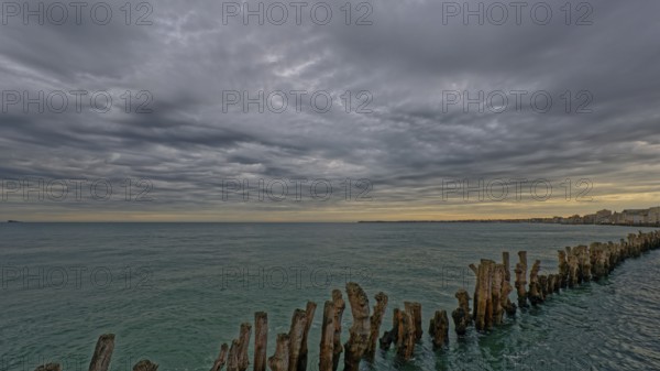 Calm sea with a row of wooden posts extending into the water under a dramatic cloudy sky, Saint-Malo, Ille-et-Vilaine, France