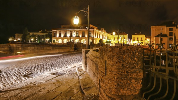 Night time on the historic landmark New Bridge Puente Nuevo of Ronda town in Spain. with running cars across the road and moving people and cars